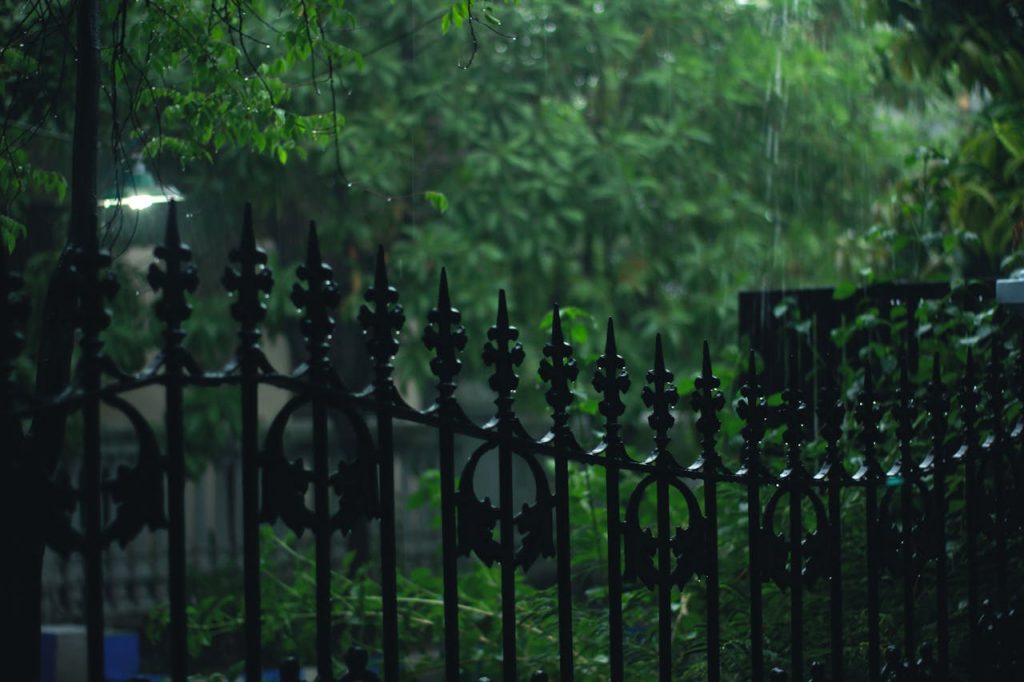 pexels photo 698772 A scenic view of a rain-soaked garden with a decorative metal fence and lush greenery, captured on a moody evening.
